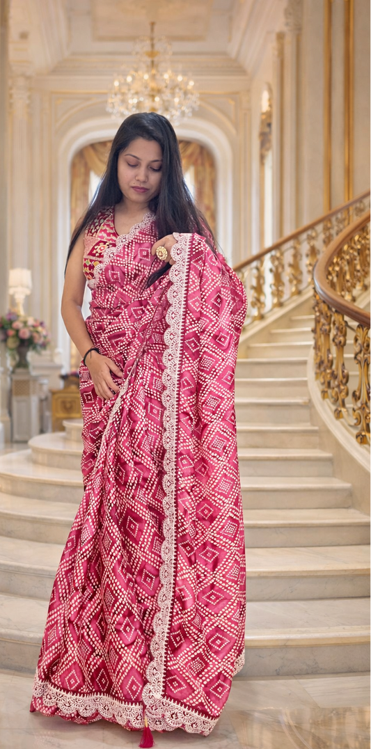 Woman in a pink saree with white patterns standing on a staircase in an elegant interior setting.