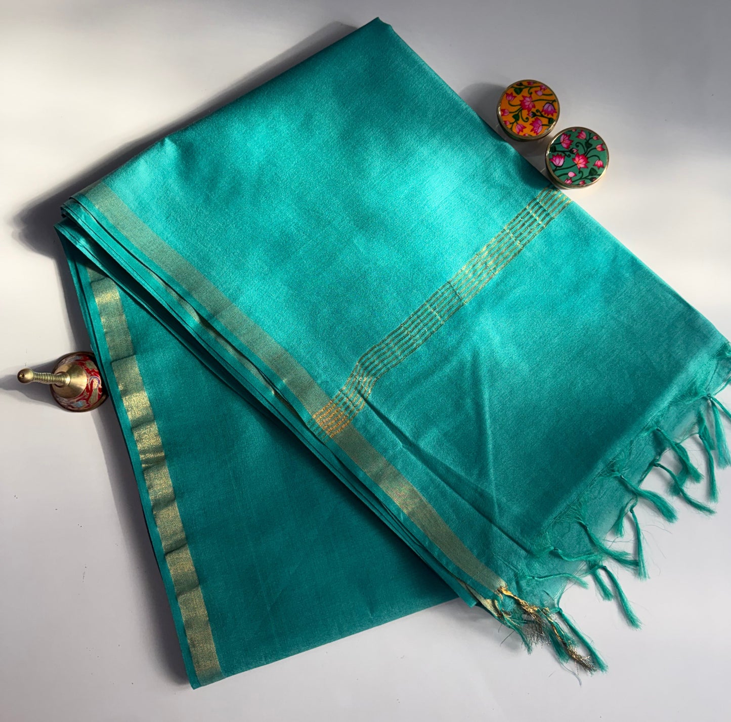 Turquoise saree with gold border and decorative buttons on a white background