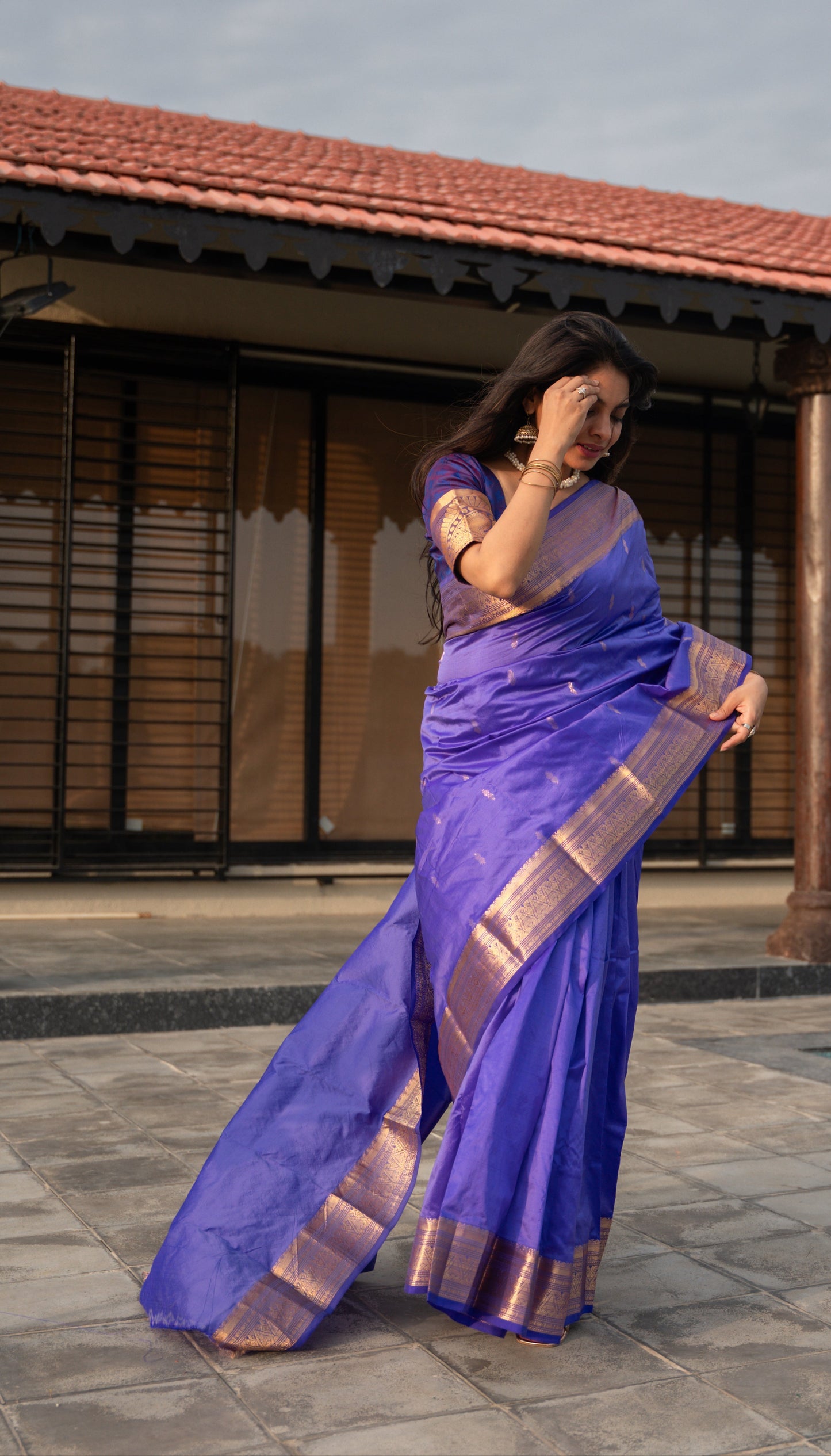 Woman in a purple saree standing on a patio with a building in the background